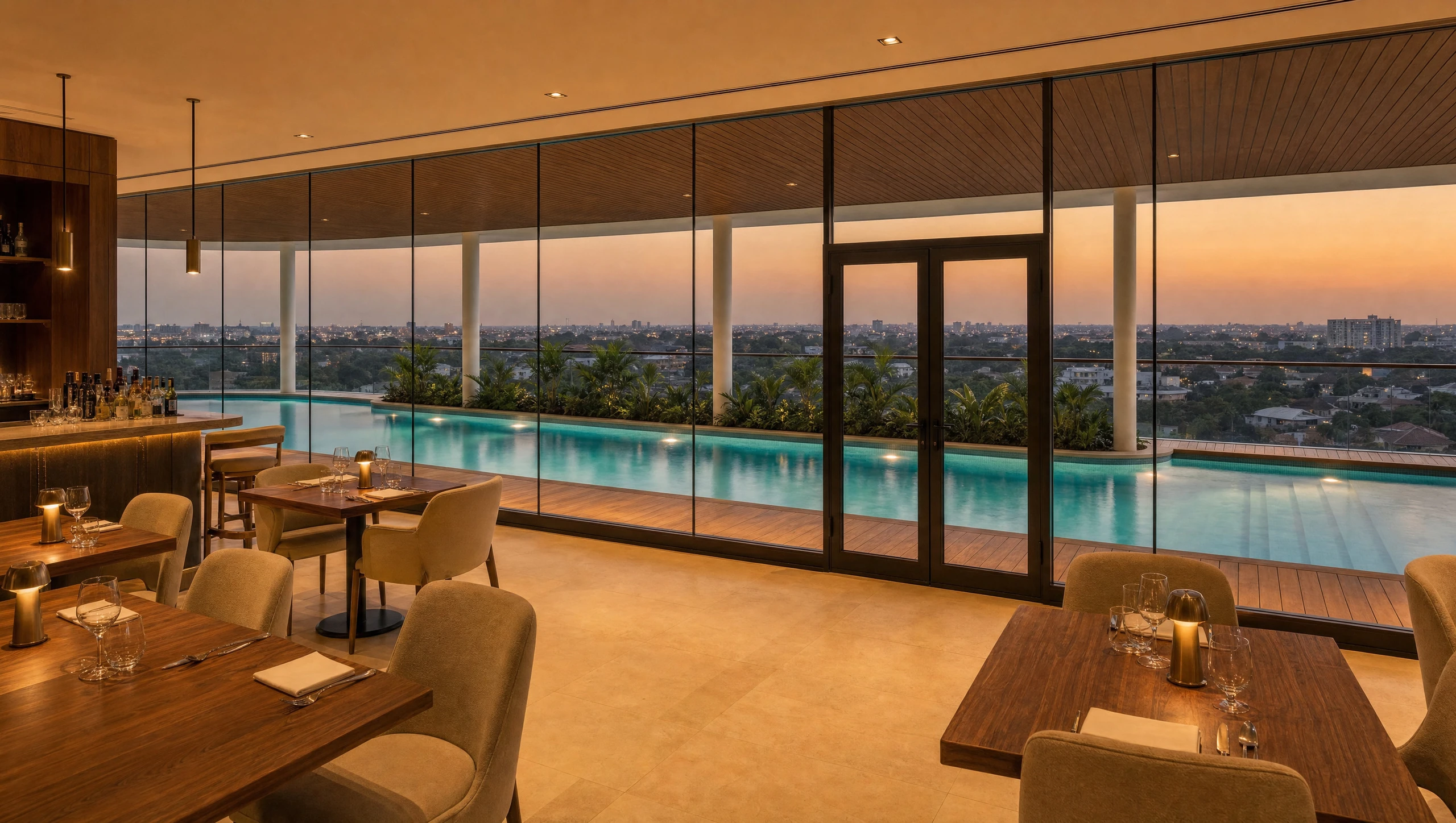 The dining room, tables set along full-height glass with the lap pool and the sunset beyond